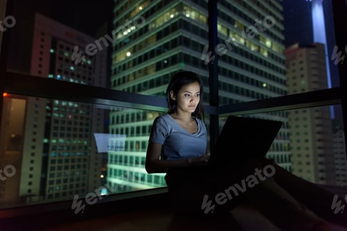 Preview: Young beautiful Asian woman using laptop against glass window wi