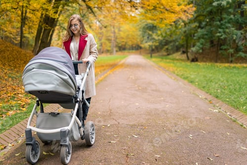 Preview: Cheerful mother with stroller walks in autumn park away from the bustle of the city