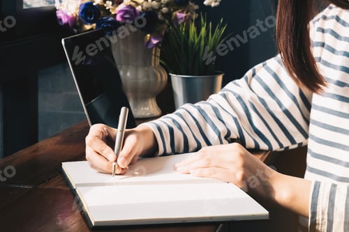Preview: Close up. Asian Female writing on a notebook with computer laptop in the coffee shop.
