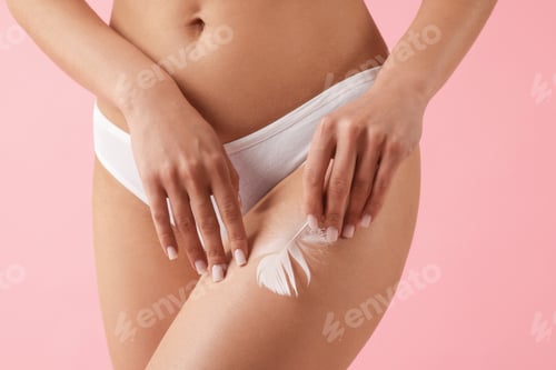 Preview: Woman with feather showing smooth skin after epilation procedure on pink background, closeup