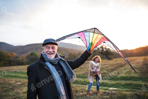 Preview: Carefree senior couple flying a kite in an autumn nature at sunset.