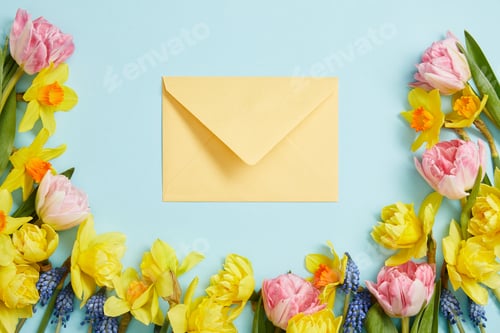 Preview: top view of pink tulips, yellow narcissus, blue hyacinths, and yellow envelope on blue