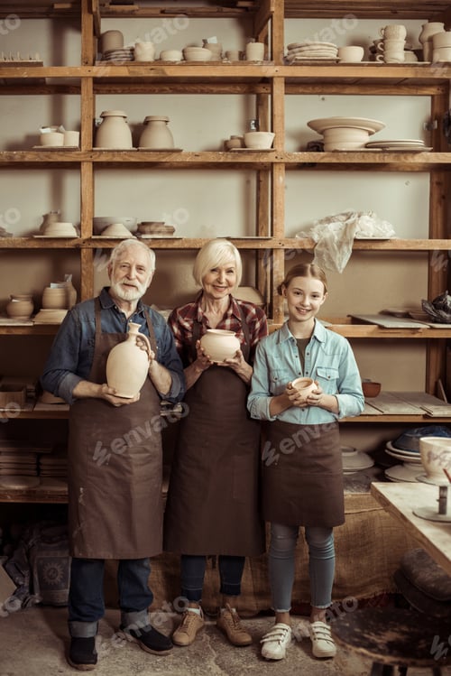 Preview: Granddaughter and grandparents standing and holding clay vase and bowls against wall with pottery
