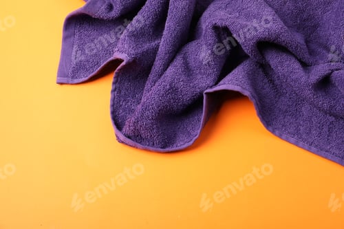 Preview: Purple terry towel on orange background, top view. Space for text