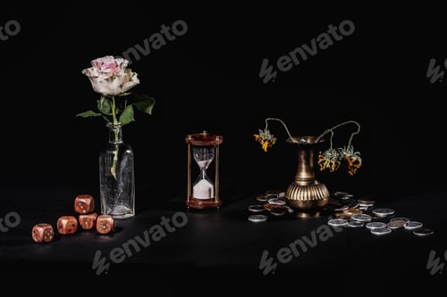 Preview: Still life shot of a timeglass, wilting flowers, money, and dice on a black background