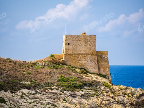 Preview: Aerial view of Xlendi Tower surrounded by rocks in background of sea in Malta