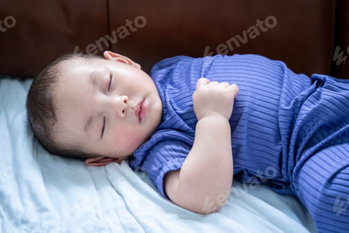 Preview: A baby is sleeping on a couch. The baby is wearing a blue outfit