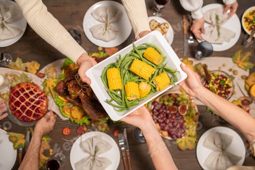 Preview: Hands of young man passing bowl with baked corn and green beans to his mother
