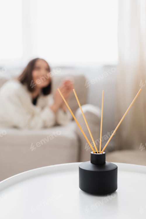 Preview: Aroma diffuser with bamboo sticks on coffee table near blurred woman in living room