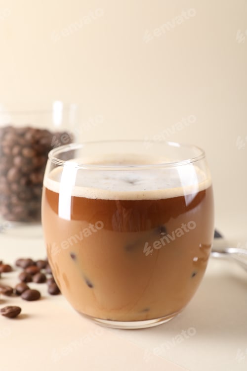Preview: Refreshing iced coffee with milk in glass and beans on beige background, space for text