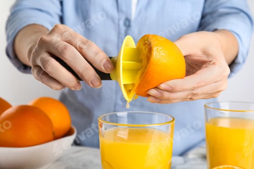 Preview: Woman squeezing orange juice at table, closeup