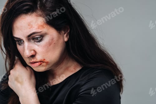 Preview: a battered woman in black clothes on an isolated gray background. Violence against women