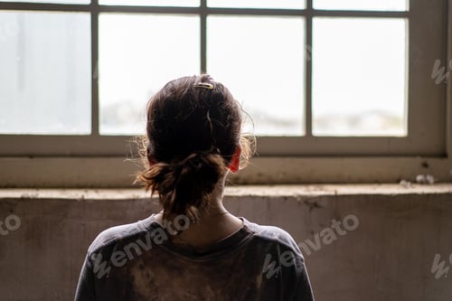 Preview: view from behind of child looking out an old window in a warehouse