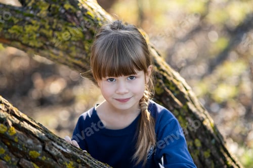 Preview: Portrait of a pretty child girl standing near a tree trunk in autumn outdoors.