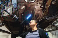 Preview: Female chinese mechanic inspecting car undercarriage with light in repair shop