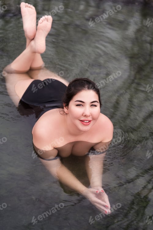 Preview: Full figured model in black swimming costume lying in geothermal water in outdoor pool at spa