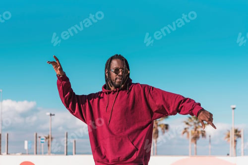 Preview: African American man in sunglasses and dreadlocks dancing on street against blue sky