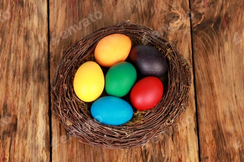 Preview: Top view closeup of colorful easter eggs in an artificial nest on a wooden table