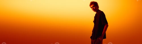 Preview: Stylish young man enjoys a moment at sunset with a vibrant orange backdrop