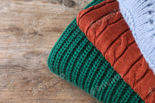 Preview: Stack of folded warm sweaters on wooden table, closeup