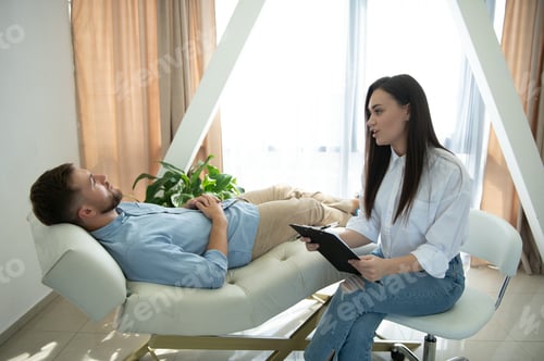 Preview: Young depressed male patient and professional female doctor with note pad. Lifestyle.