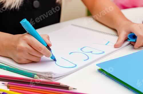 Preview: Hands of a child writing letters with blue marker on white. English learning concept