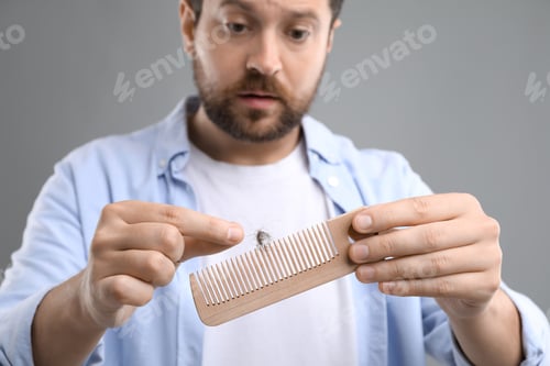 Preview: Sad man taking his lost hair from comb on gray background, closeup. Alopecia problem