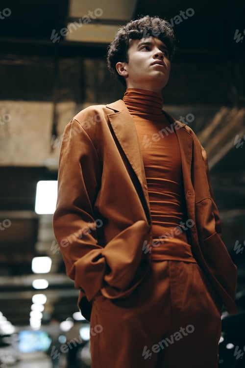 Preview: Young man in a stylish orange outfit standing confidently in a modern parking garage