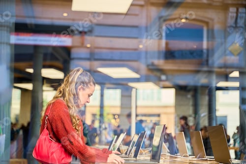 Preview: Young Caucasian woman browsing laptops in electronics store