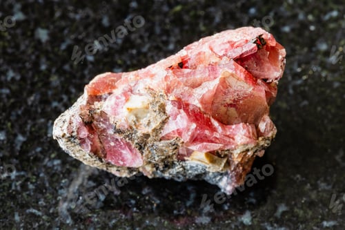 Preview: sample of raw rhodonite rock on black granite