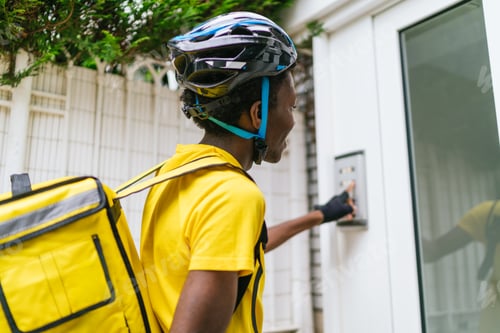 Preview: Food delivery cyclist pressing a doorbell while wearing a helmet and a yellow delivery bag