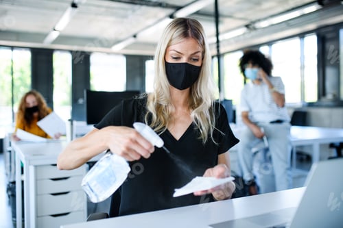 Preview: Young woman with face mask back at work in office after lockdown, disinfecting hands