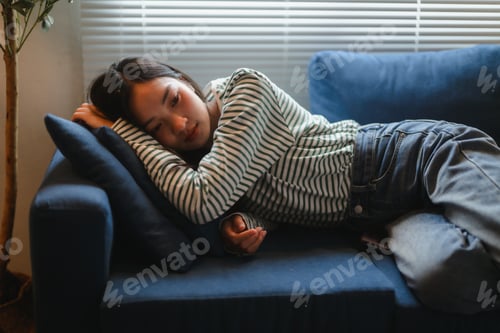 Preview: Sad young Asian woman is lying on the sofa at home