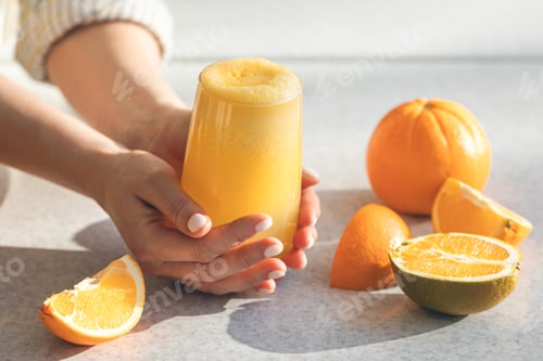 Preview: Freshly squeezed orange juice in female hands, close up.