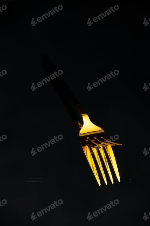 Preview: Half shot of elegant shiny golden fork on black blurred background with free space in side view