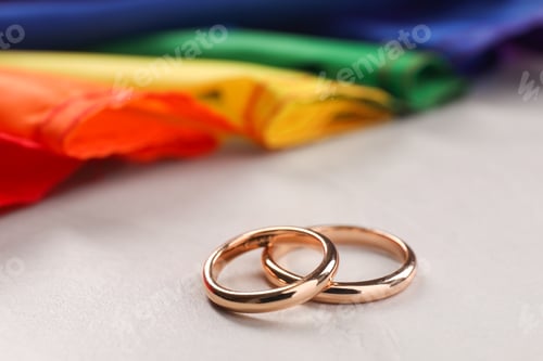 Preview: Rainbow LGBT flag and wedding rings on white background, closeup