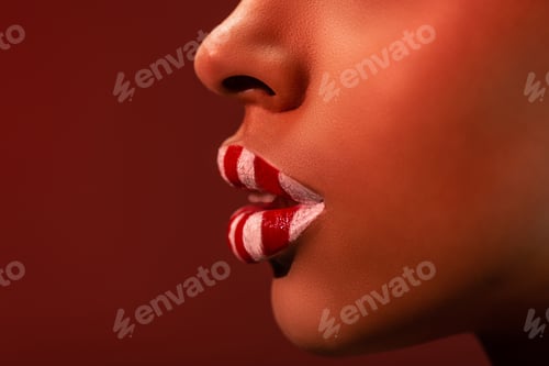 Preview: close-up partial view of beautiful female face with red and white striped lips isolated on burgundy