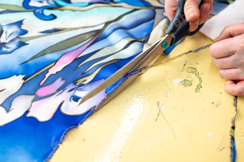 Preview: the hands of a man cutting a piece of floral fabric with scissors, batik