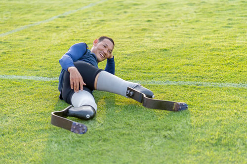 Preview: Sport man athlete prosthesis legs lie down on grass field to relax also look at camera with smiling
