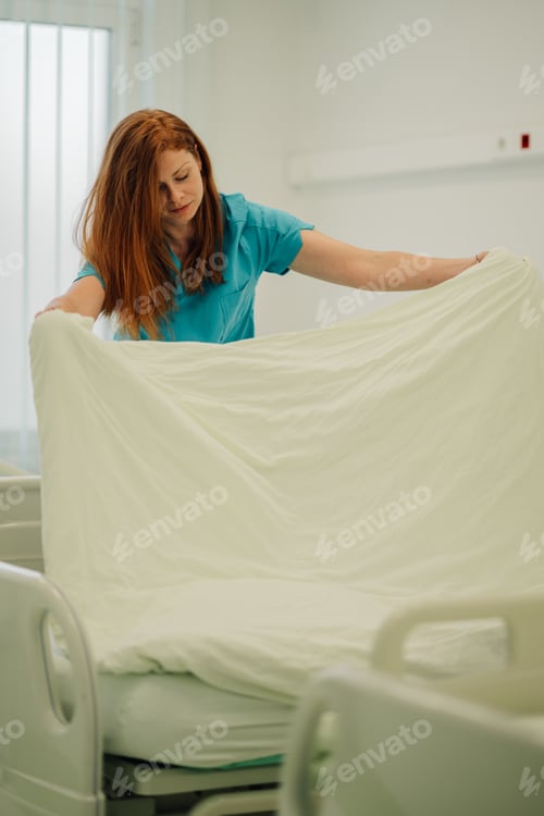 Preview: Nurse preparing a hospital bed with fresh linens and blankets.