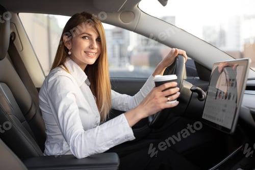 Preview: caucasian business woman sitting in modern electric car and drinking take away coffee