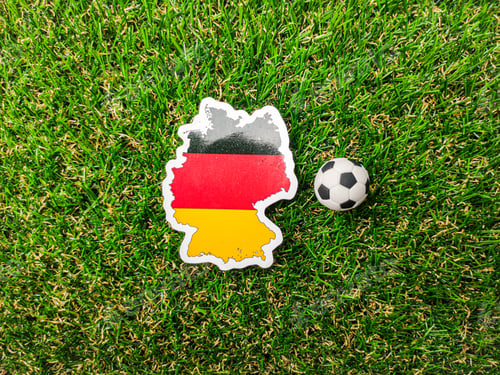Preview: A ball and German flag sticker is on a green field.