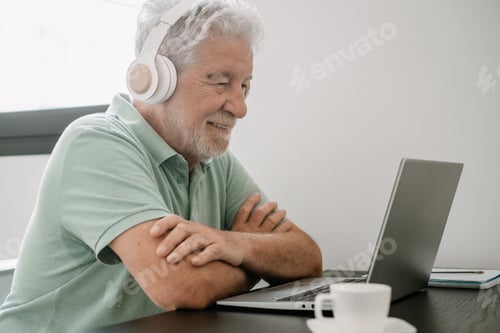 Preview: Video call concept. Senior smiling businessman sitting at home desk working online on laptop
