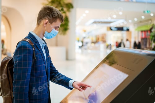 Preview: young man in the mall looks at the monitor in a mask