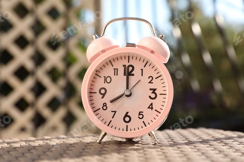 Preview: Pink alarm clock on table outdoors at sunny morning