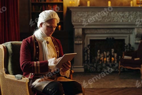 Preview: Caucasian Young Adult Man Wearing Baroque Costume Using Digital Tablet Indoors