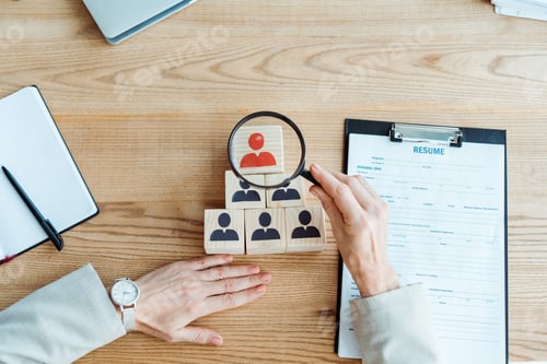 Preview: top view of recruiter holding magnifier near cube and clipboard in office