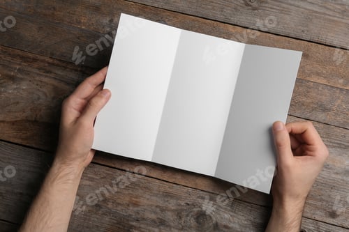 Preview: Man with blank brochure on wooden background, above view. Mock up for design