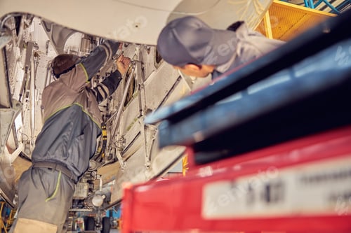 Preview: Two men mechanics examine an open jet part in an aircraft hangar