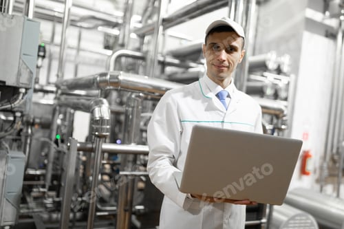 Preview: Portrait of man in a white robe and a cap standing in production department of dairy factory with
